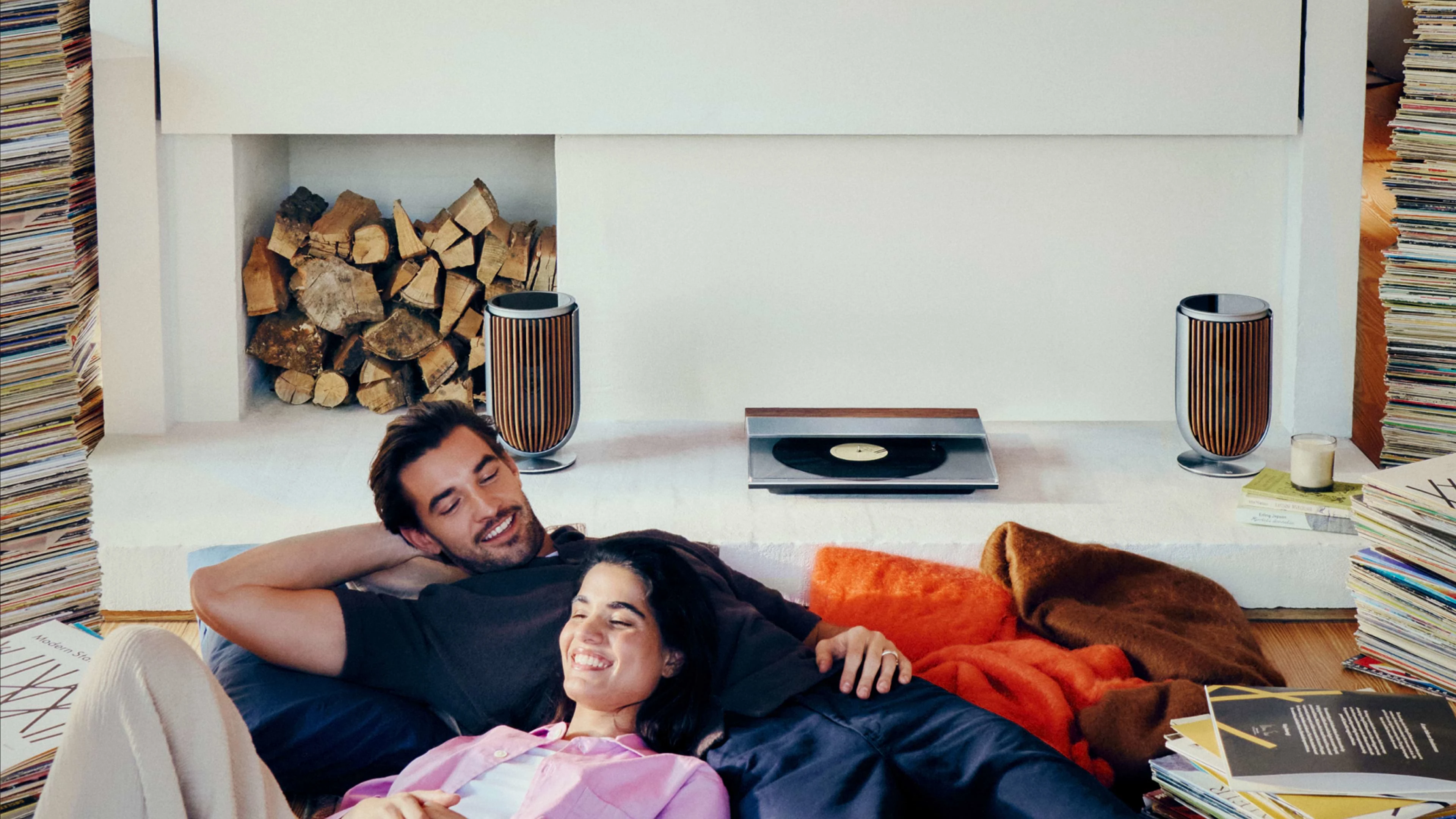 Two people sitting at a fireplace with the Beogram 3000c and Beolab 8 in the background