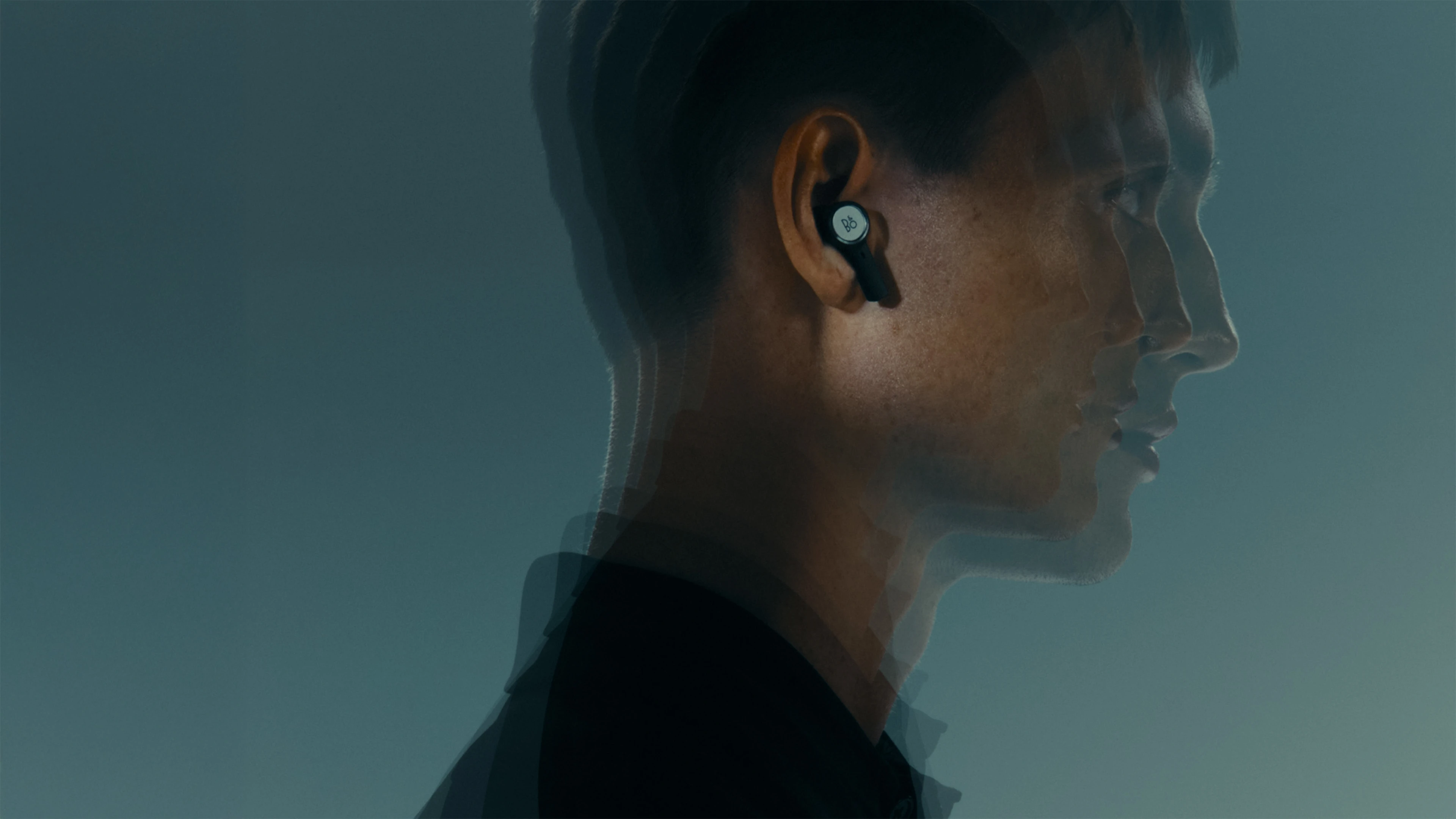 A man is wearing a natural aluminium Beoplay Eleven wireless earbuds